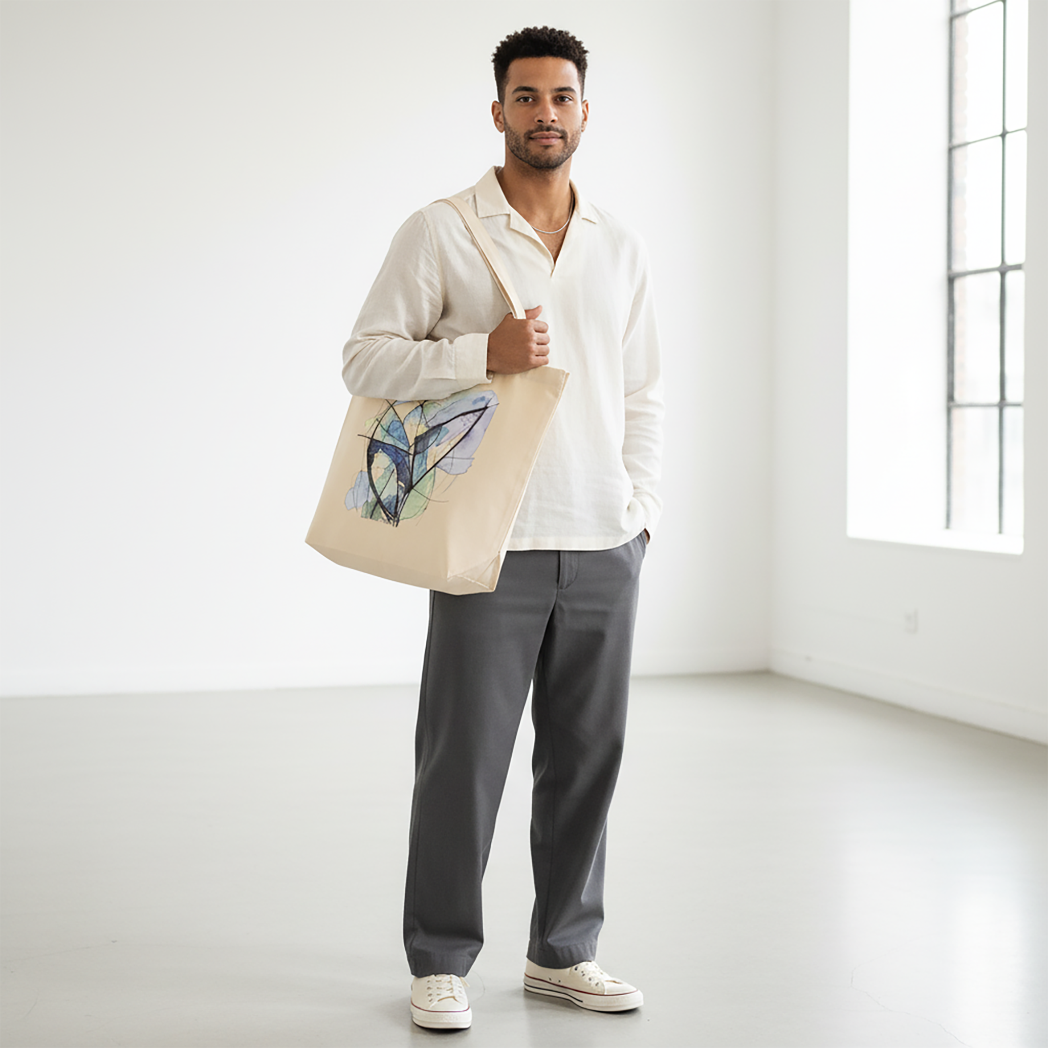 Abstract Butterfly Tote from Later&Before. Crafted from premium 100% organic cotton, this high-quality essential is as durable as it is eco-conscious. It features an artistic abstract print in cool blue and green tones. Spacious and sturdy, it’s ideal for everything from market days to daily commutes.
A man stands in a white studio, wearing an off-white collared shirt and grey trousers. He is holding a cream Later&Before organic cotton tote bag on his shoulder.